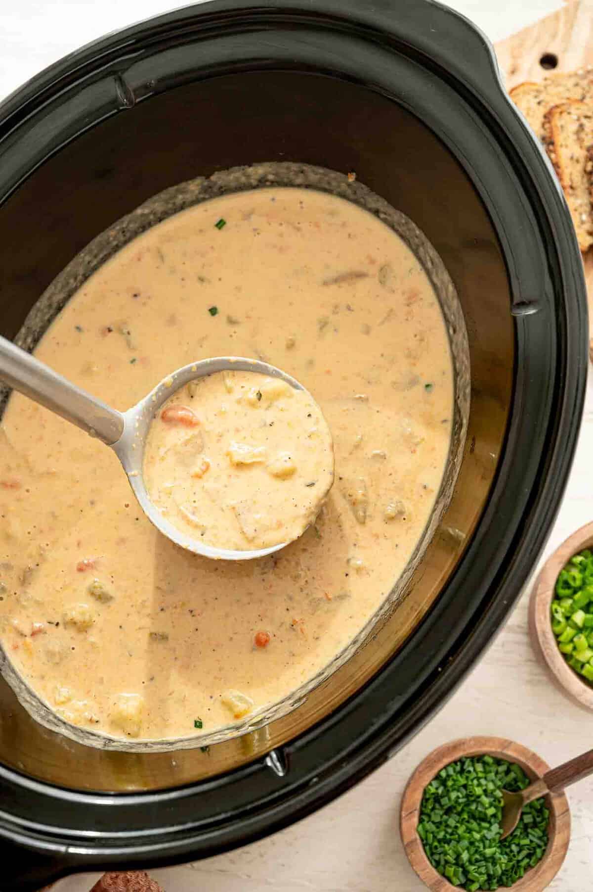 Cheddar and bacon potato soup being ladled out of a crockpot.