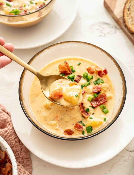 A bowl of cheddar and bacon potato soup with a spoon lifting out a bite.