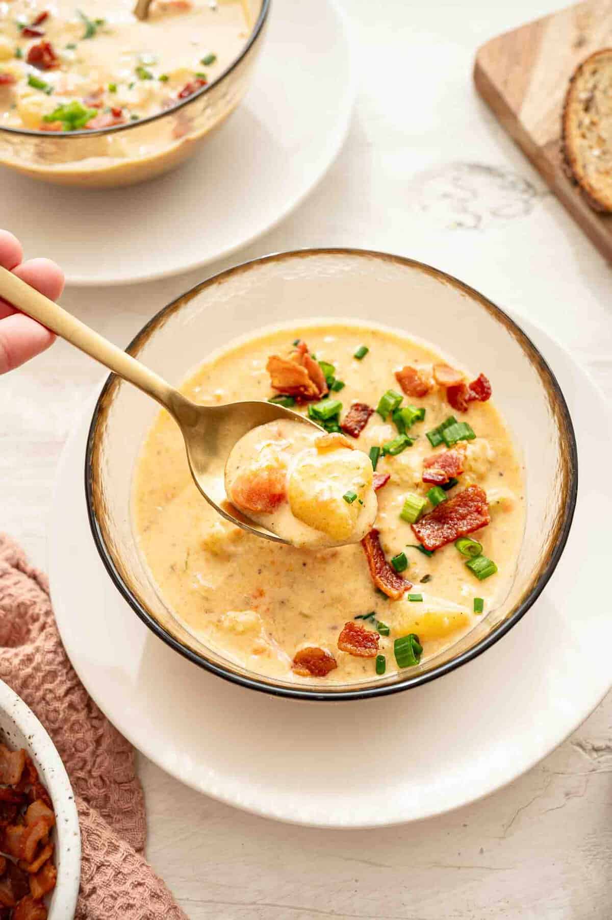 A bowl of cheddar and bacon potato soup with a spoon lifting out a bite.