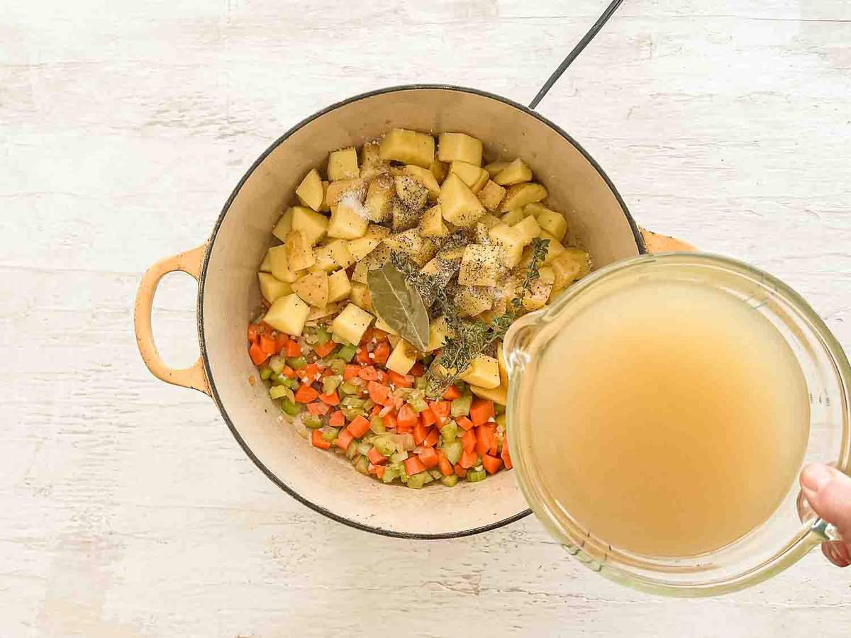 Chicken stock being poured into a pot with other potato soup ingredients already in it.