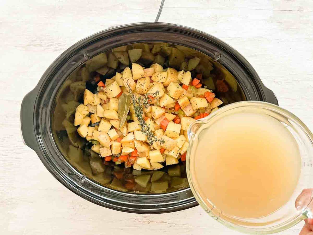 Potato soup ingredients in a crockpot with chicken stock being poured into it.