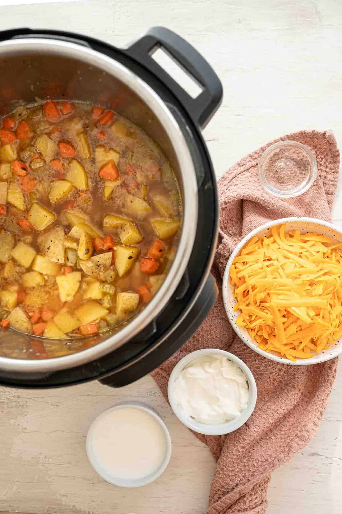 Potato soup ingredients in an Instant Pot with other ingredients in bowls next to it.