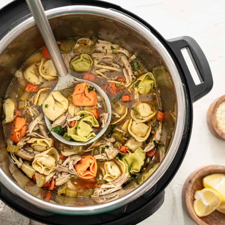 Chicken tortellini soup on an Instant Pot with small bowls of Parmesan cheese and lemon wedges next to it.