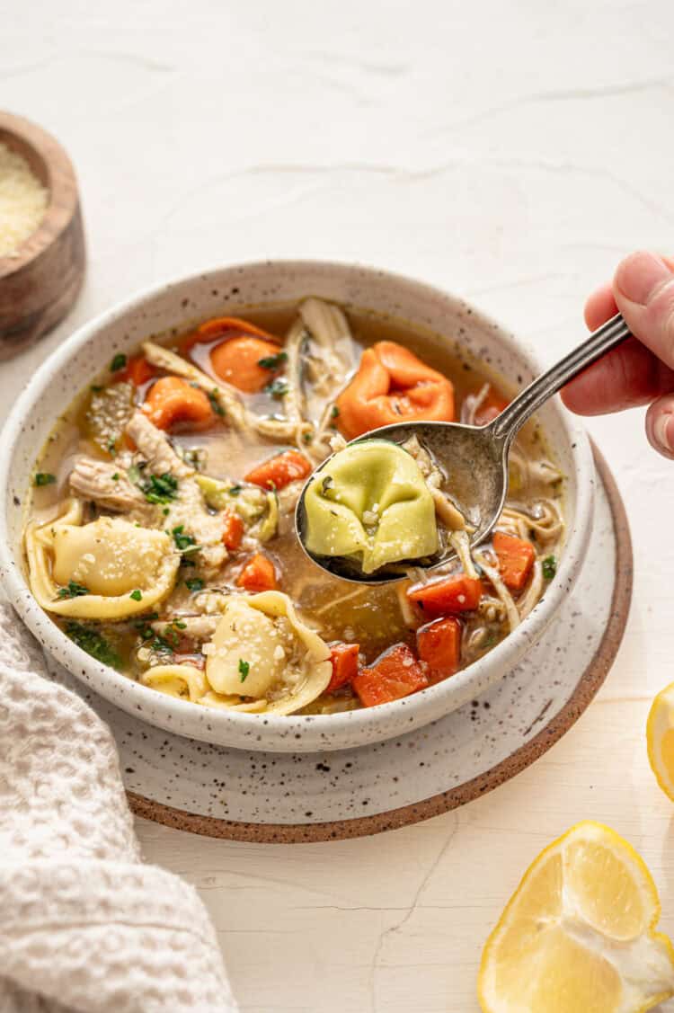 Chicken tortellini soup on a bowl with fresh chopped parsley and Parmesan cheese on top.
