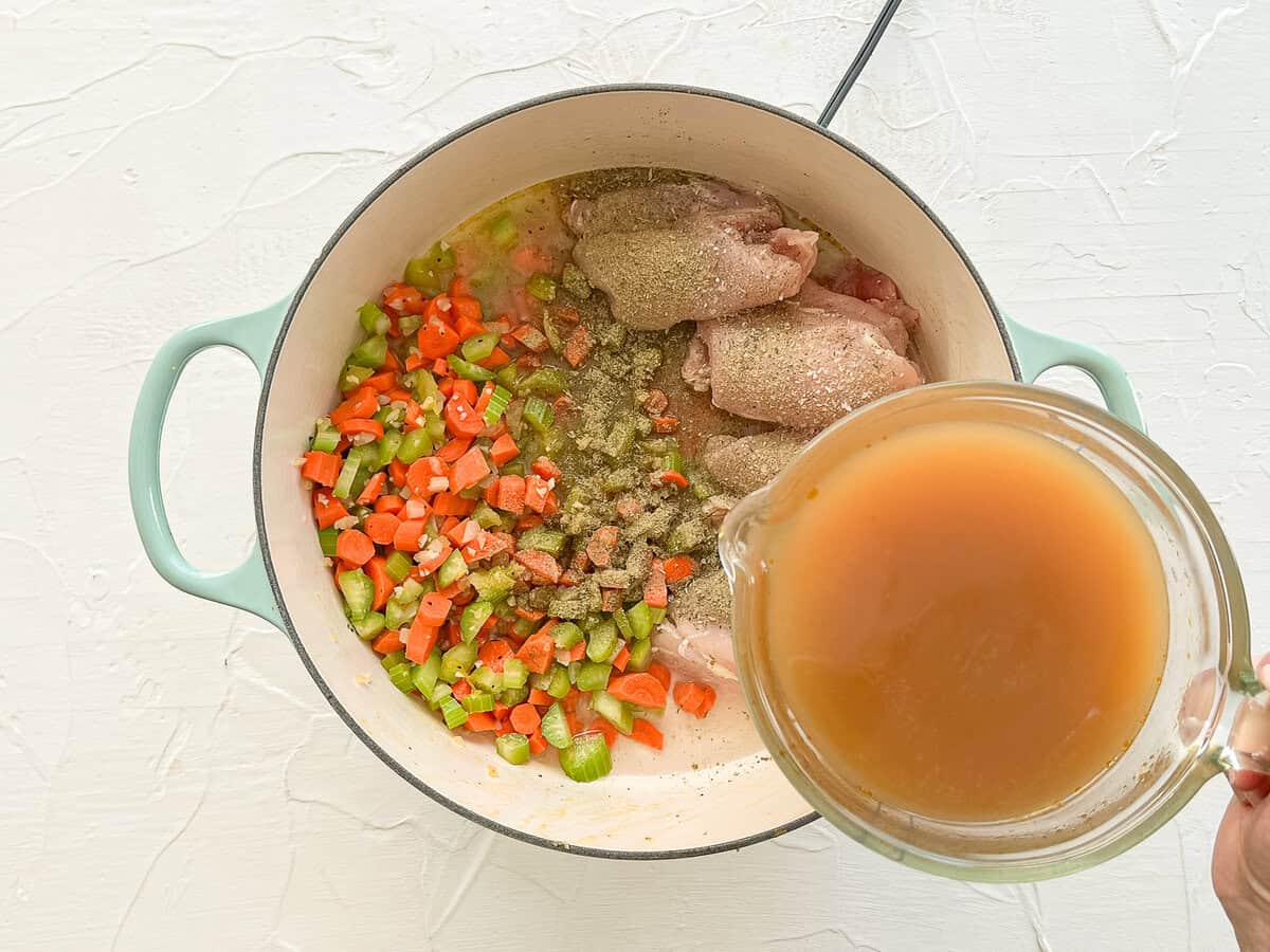 Chicken broth being poured into a large pot with other ingredients for chicken tortellini soup.