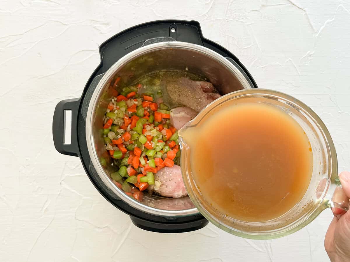 Chicken broth being poured into an Instant Pot with the other ingredients for chicken tortellini soup.