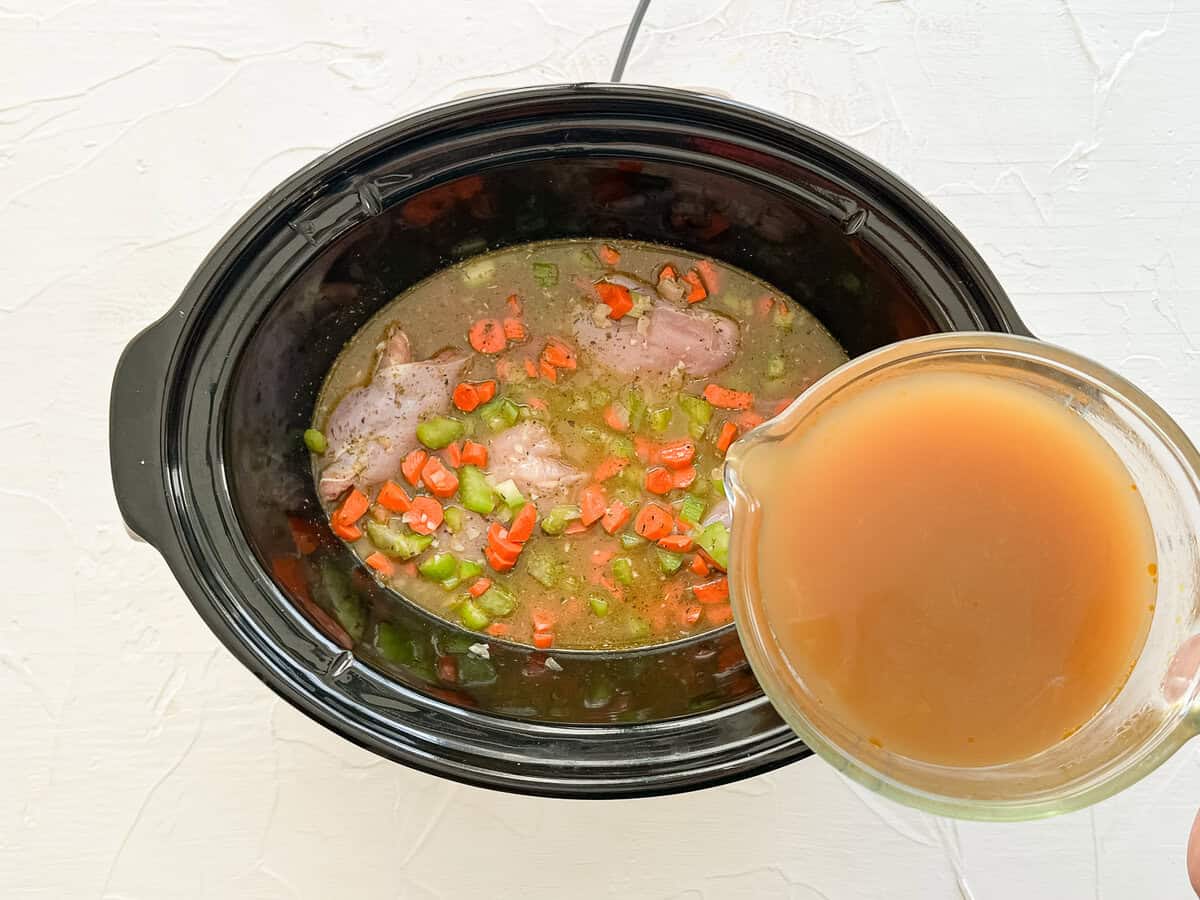 Chicken broth being poured into a slow cooker with the rest of the ingredients for chicken tortellini soup.