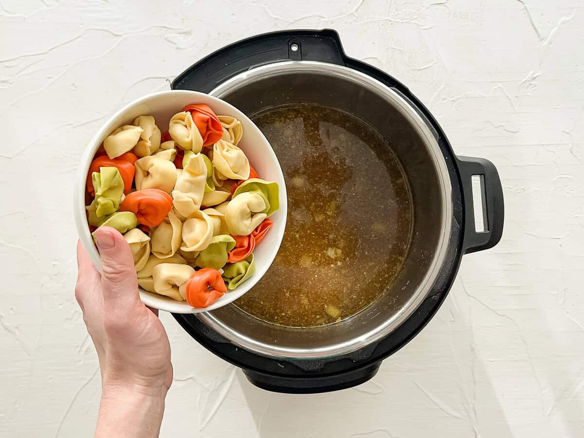 Cheese tortellini being dumped into an Instant Pot for chicken tortellini soup.