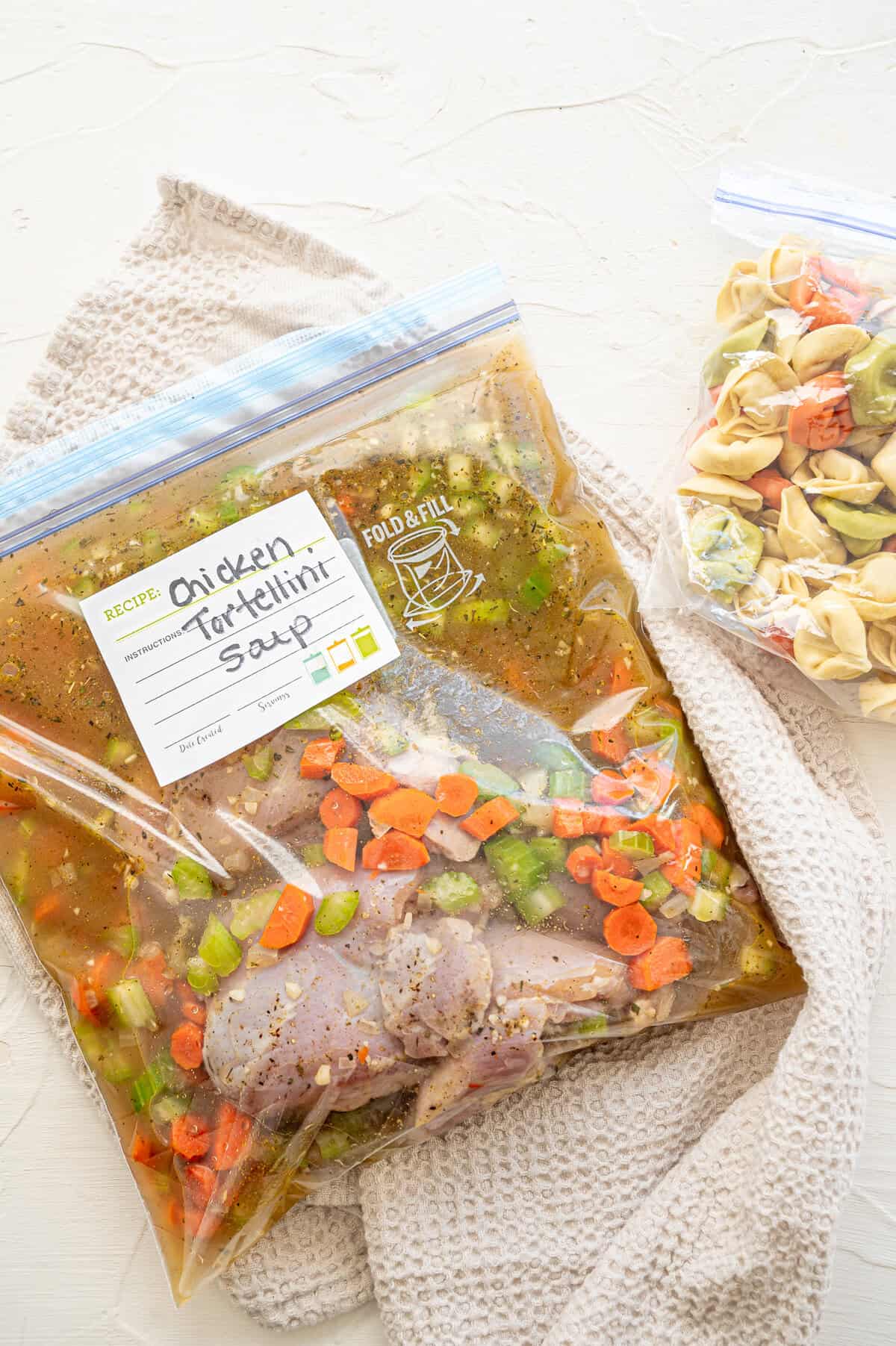 Cheese tortellini in a small freezer bag next to a large freezer bag with the rest of the ingredients for chicken tortellini soup.