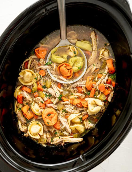 Chicken tortellini soup in a slow cooker being served with a ladle.