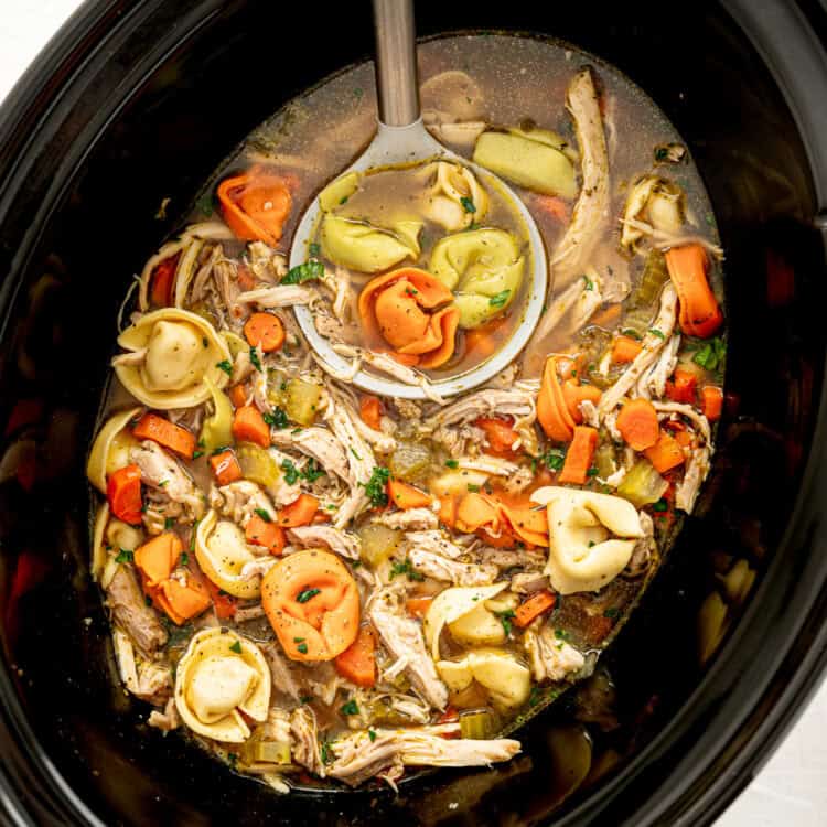 Chicken tortellini soup in a slow cooker being served with a ladle.