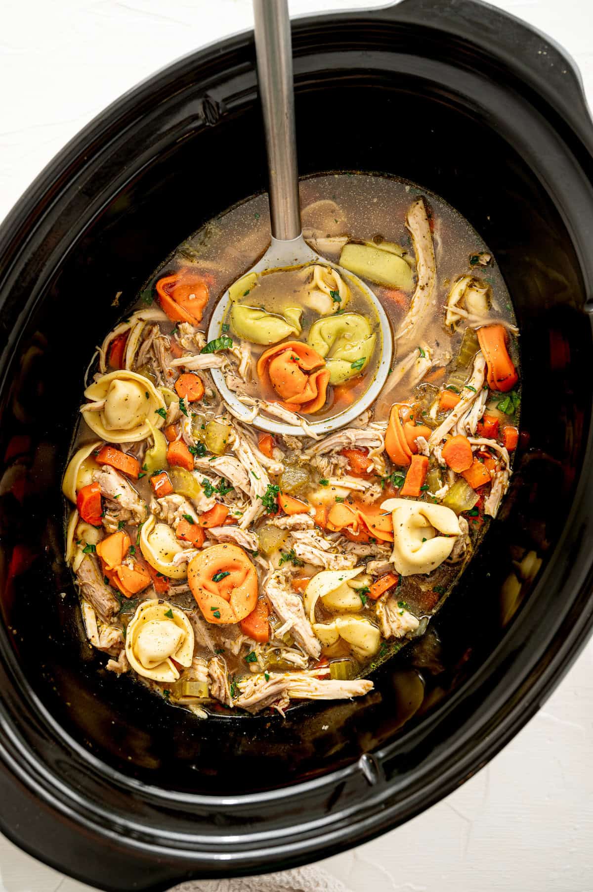 Chicken tortellini soup in a slow cooker being served with a ladle.