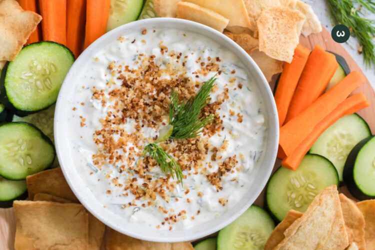 Fried dill pickle dip in a bowl with fresh dill on top and veggies around the side of it.