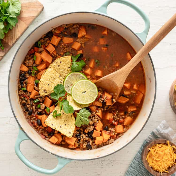 Turkey and sweet potato chili in a pot ready to serve with lime slices, cilantro and tortilla chips on top.