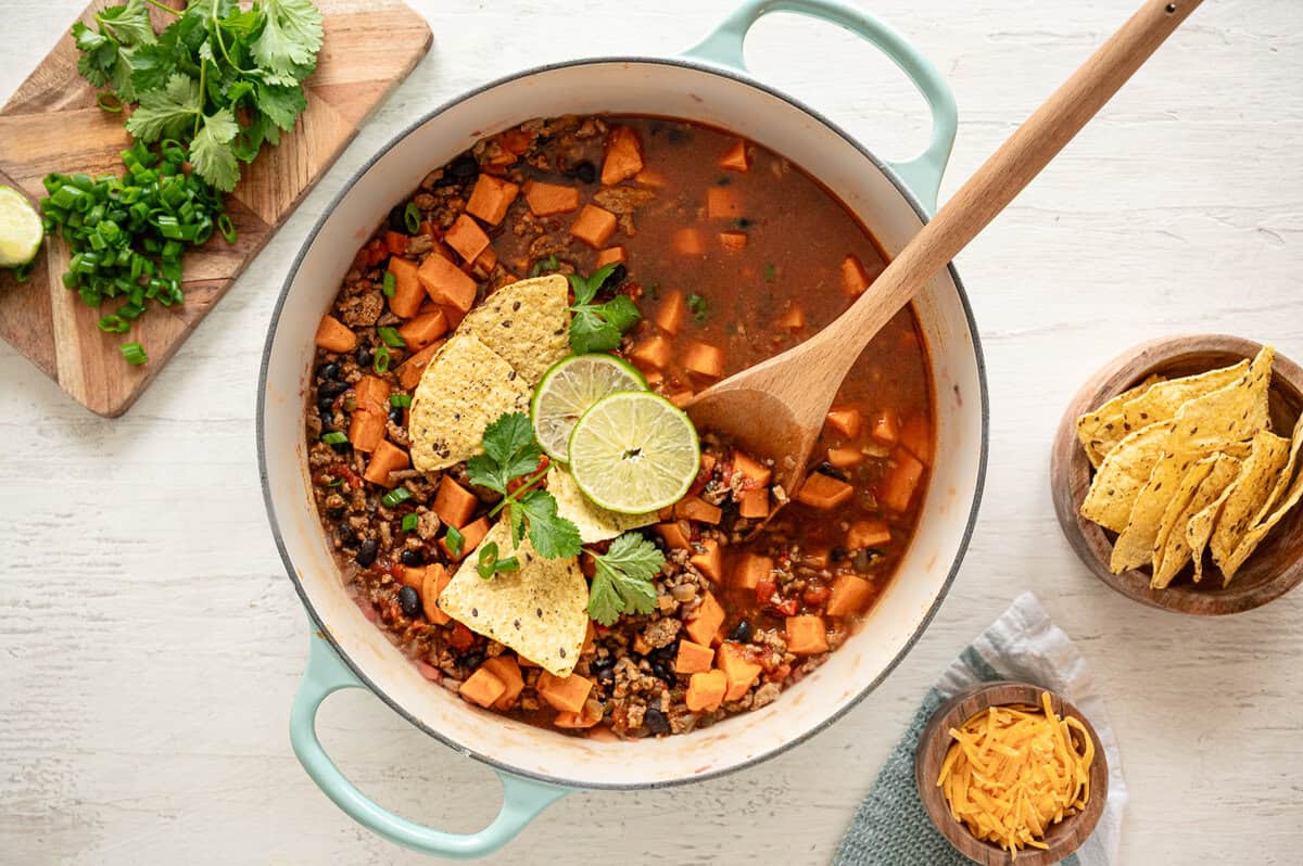 Turkey and sweet potato chili in a pot ready to serve with lime slices, cilantro and tortilla chips on top.