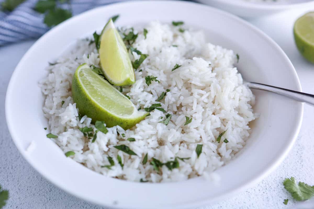 Coconut rice in a bowl served with fresh chopped cilantro and lime wedges on top.