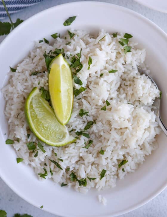 A white bowl of coconut rice with two lime wedges on top.