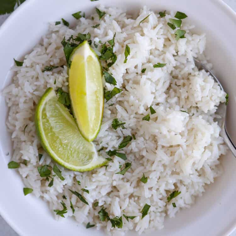 A white bowl of coconut rice with two lime wedges on top.