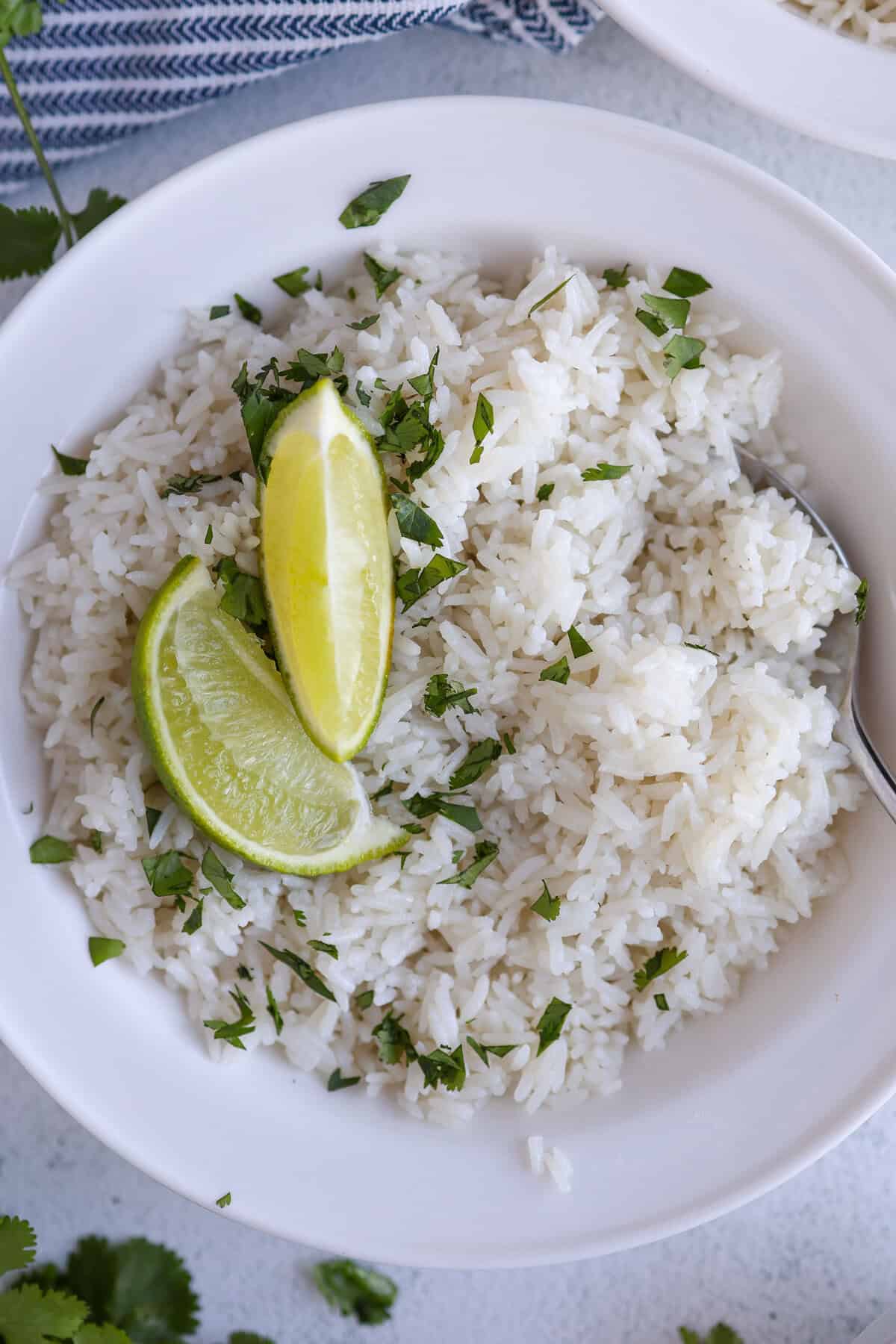 A white bowl of coconut rice with two lime wedges on top.