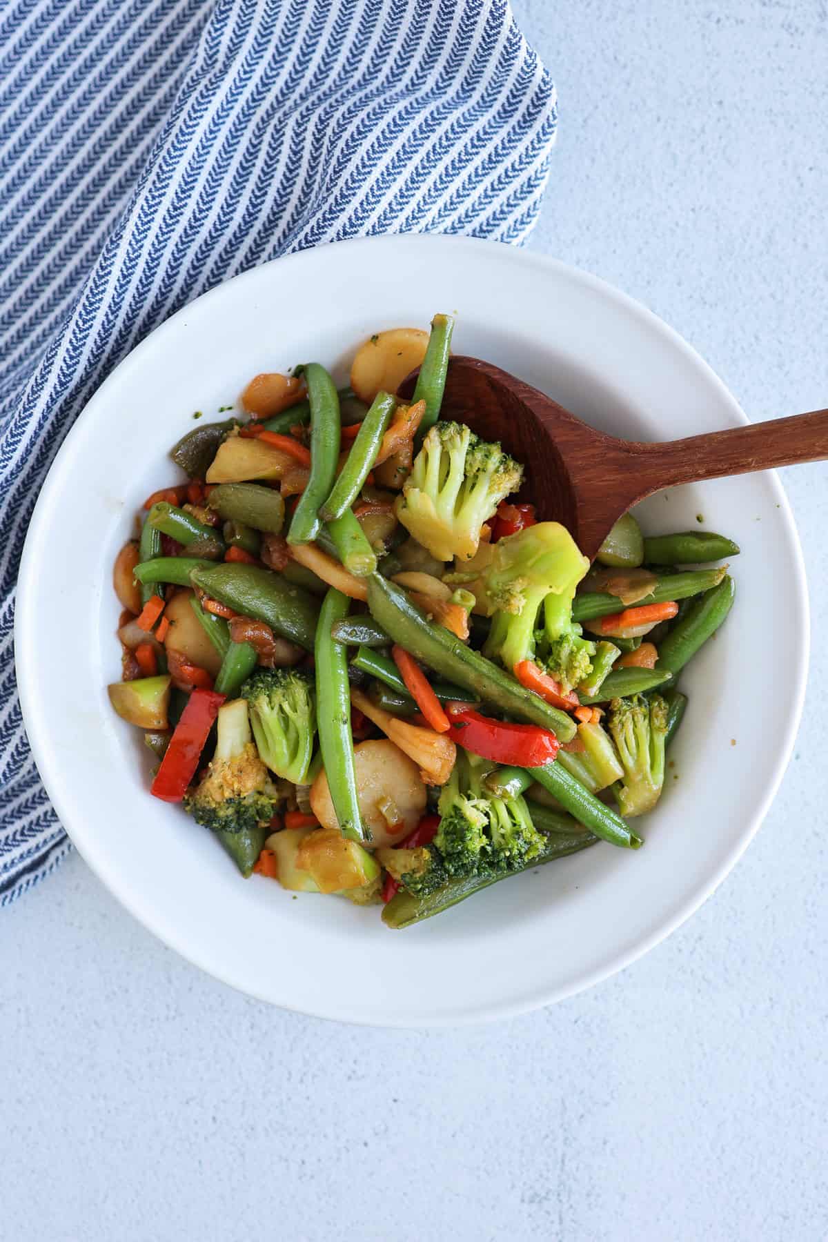 A wooden spoon in a bowl of stir-fry veggies.