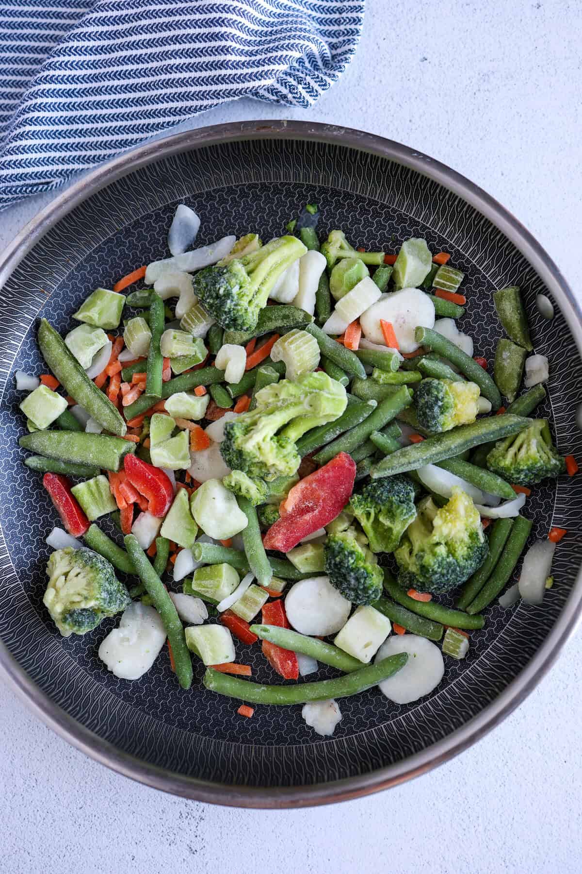 Frozen stir-fry veggies in a skillet waiting to be sauteed.