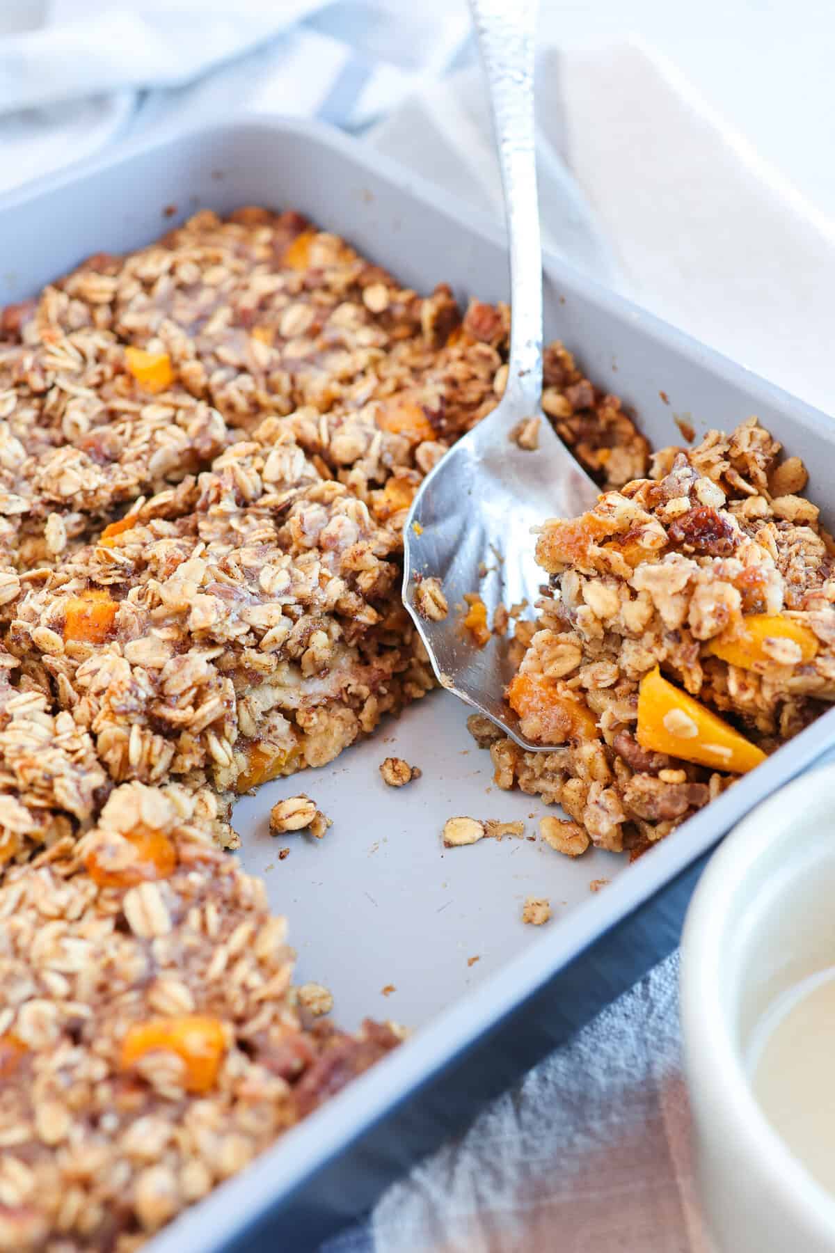 Peaches and cream baked oatmeal in a baking dish with a serving missing.