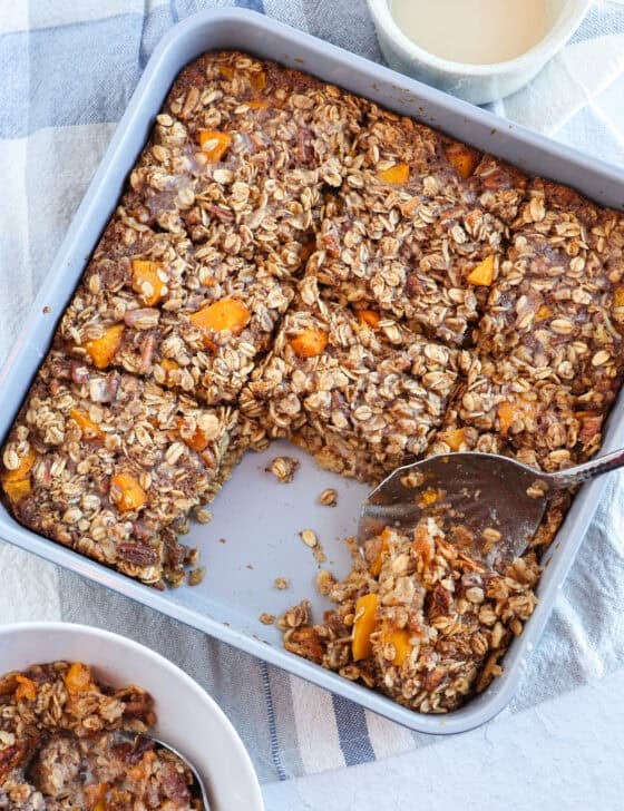 A spoon scooping a serving out of a pan of peaches and cream baked oatmeal.