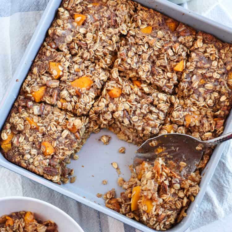 A spoon scooping a serving out of a pan of peaches and cream baked oatmeal.