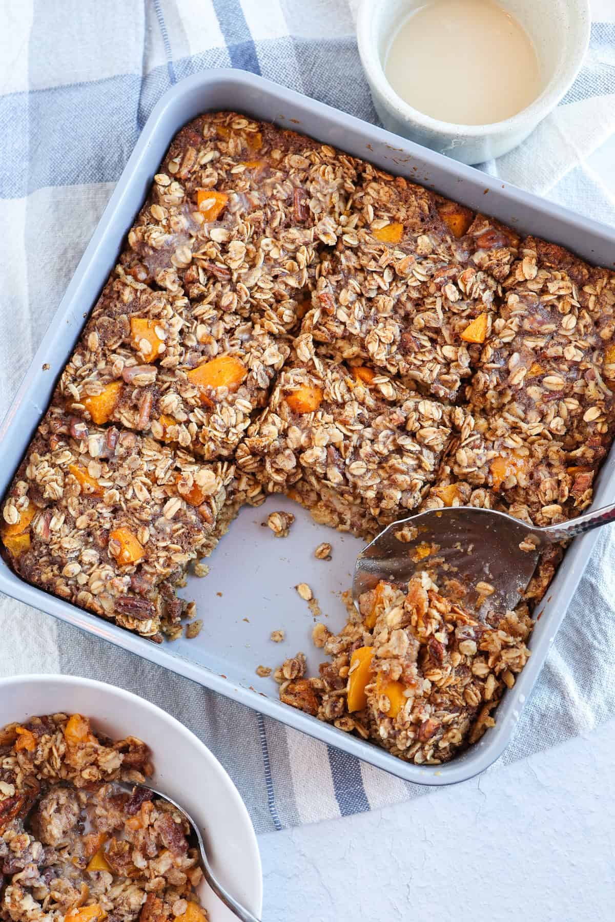 A spoon scooping a serving out of a pan of peaches and cream baked oatmeal.