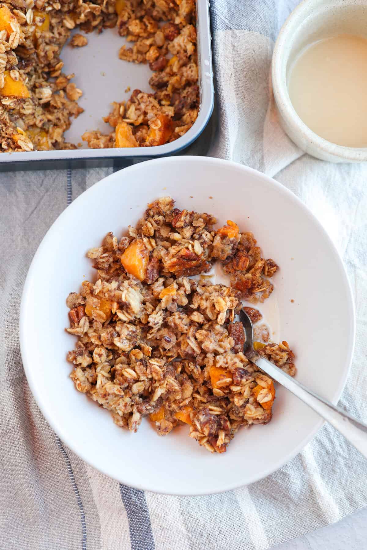 A bowl with peaches and cream baked oatmeal and some milk in it.