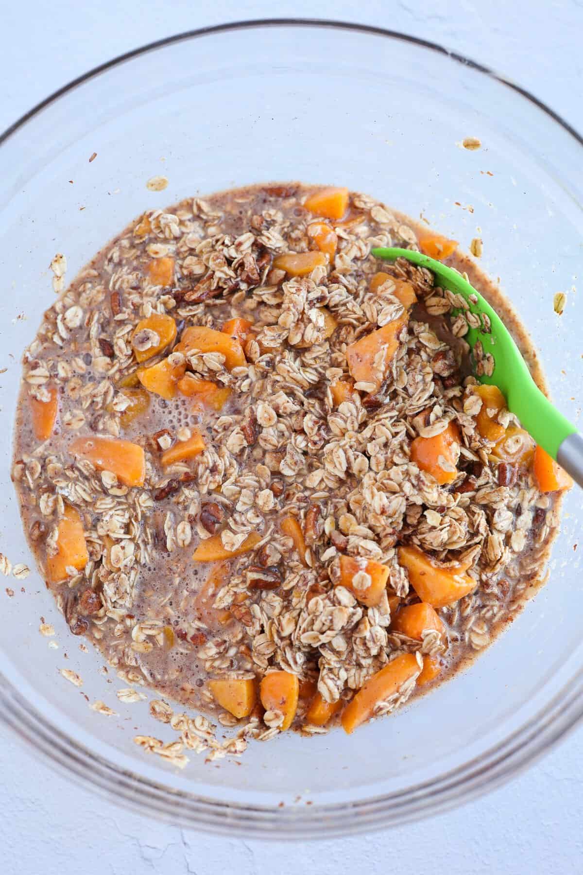 A glass mixing bowl with ingredients for peaches and cream baked oatmeal being stirred together.