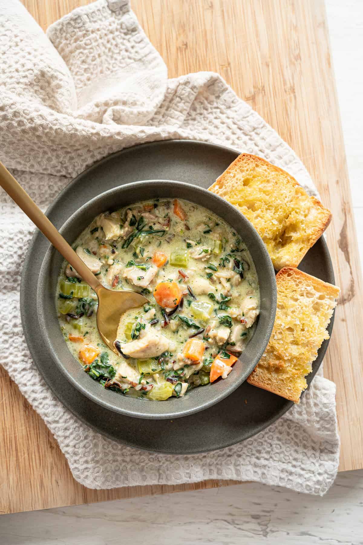 Boursin chicken and wild rice soup served in a gray bowl with crusty bread on the side.