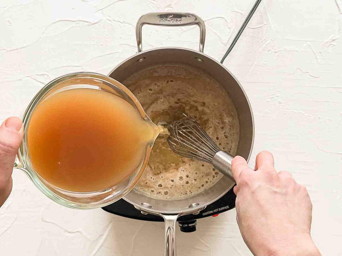 Chicken broth being whisked into a roux in a saucepan.