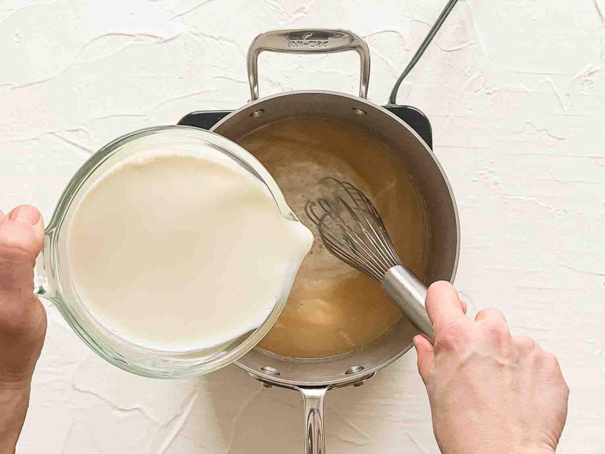 Milk being whisked into a saucepan while making homemade alfredo sauce.