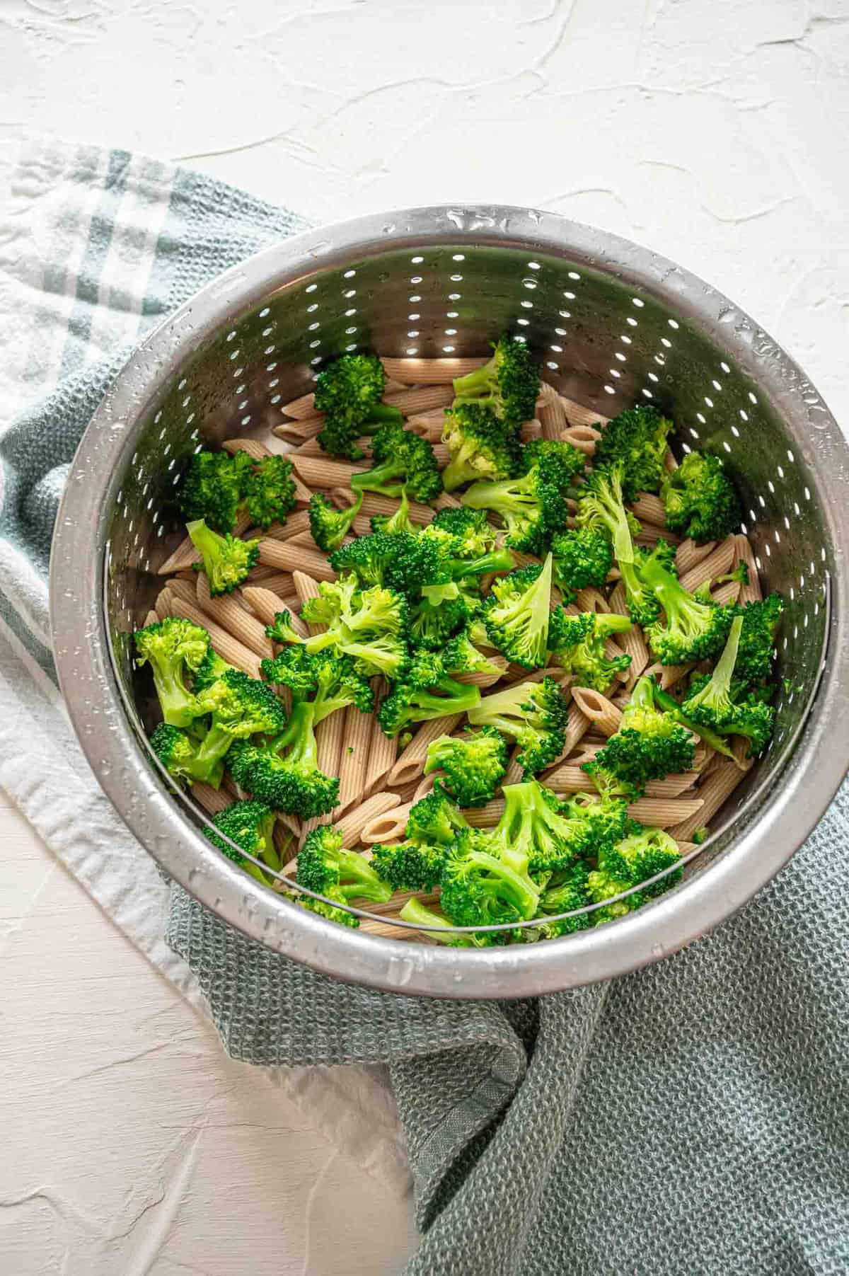 Whole grain penne pasta and broccoli florets in a steamer basket.