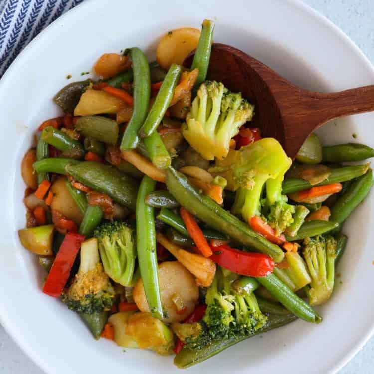 Stir fry veggies in a bowl with a wooden spoon.