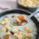 A spoon with clam chowder on it from the bowl beneath it.