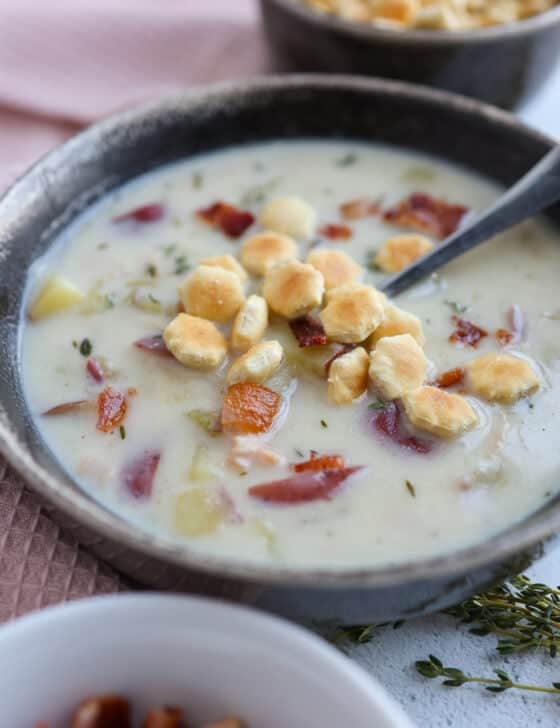 A bowl of clam chowder with bowls of oyster crackers and chopped bacon next to it.