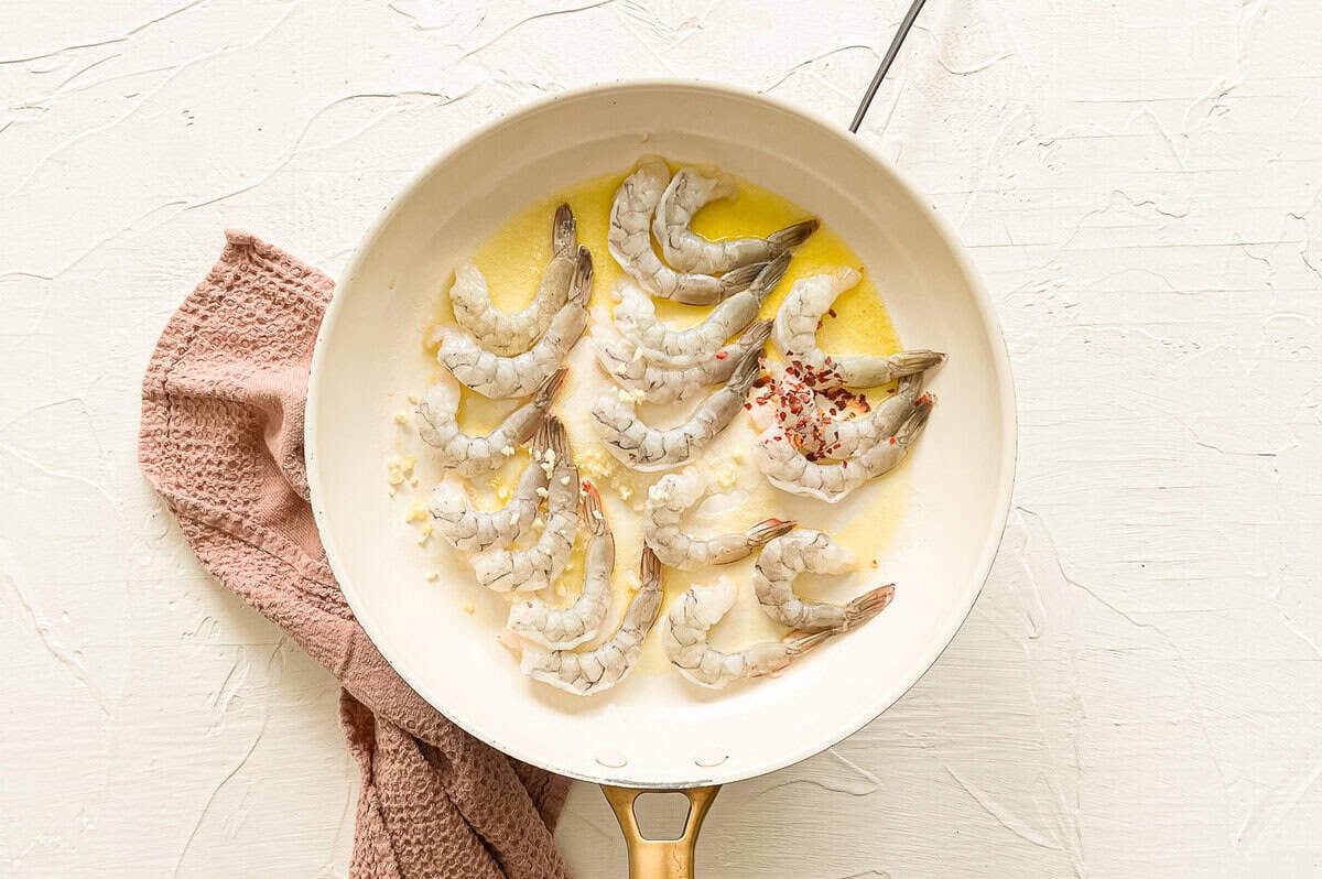 Shrimp being sauteed in butter and garlic in a skillet.