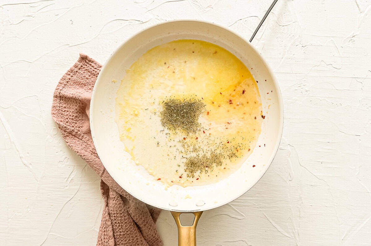 Melted butter in a skillet with Italian seasoning, minced garlic, and red pepper flakes being added.