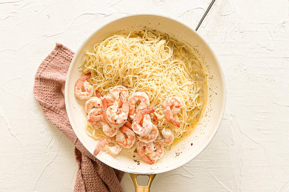 Cooked shrimp and cooked spaghetti noodles dumped in a skillet with scampi sauce.