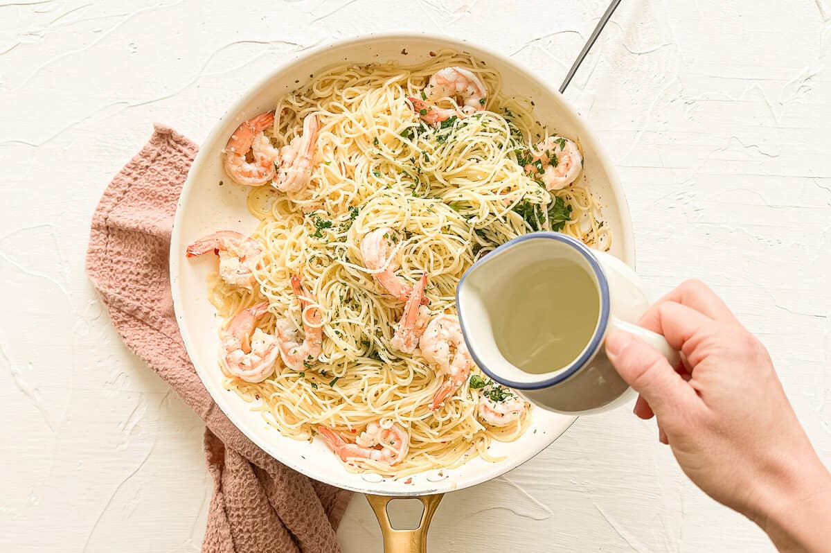 Reserved pasta water being poured on shrimp scampi pasta to make it glossy.