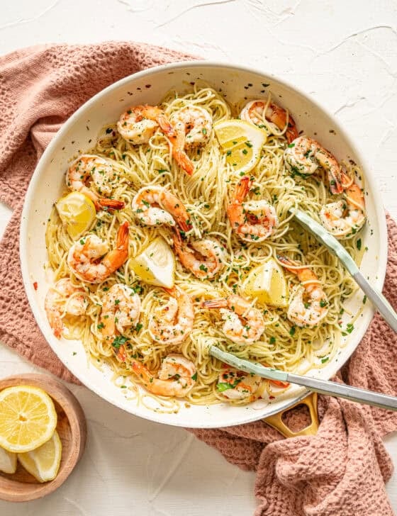 Shrimp scampi pasta served from a skillet with fresh parsley and lemon wedges on top.