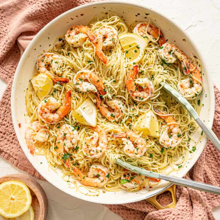 Shrimp scampi pasta served from a skillet with fresh parsley and lemon wedges on top.