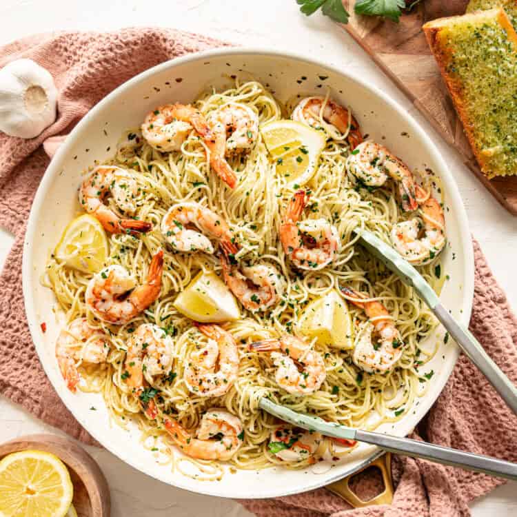 Shrimp scampi pasta being served with lemon wedges, chopped fresh parsley, and Texas toast.