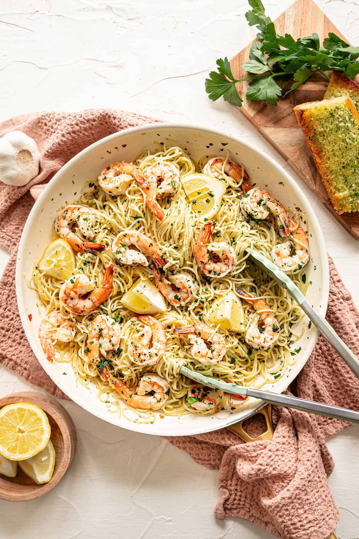 Shrimp scampi pasta being served with lemon wedges, chopped fresh parsley, and Texas toast.