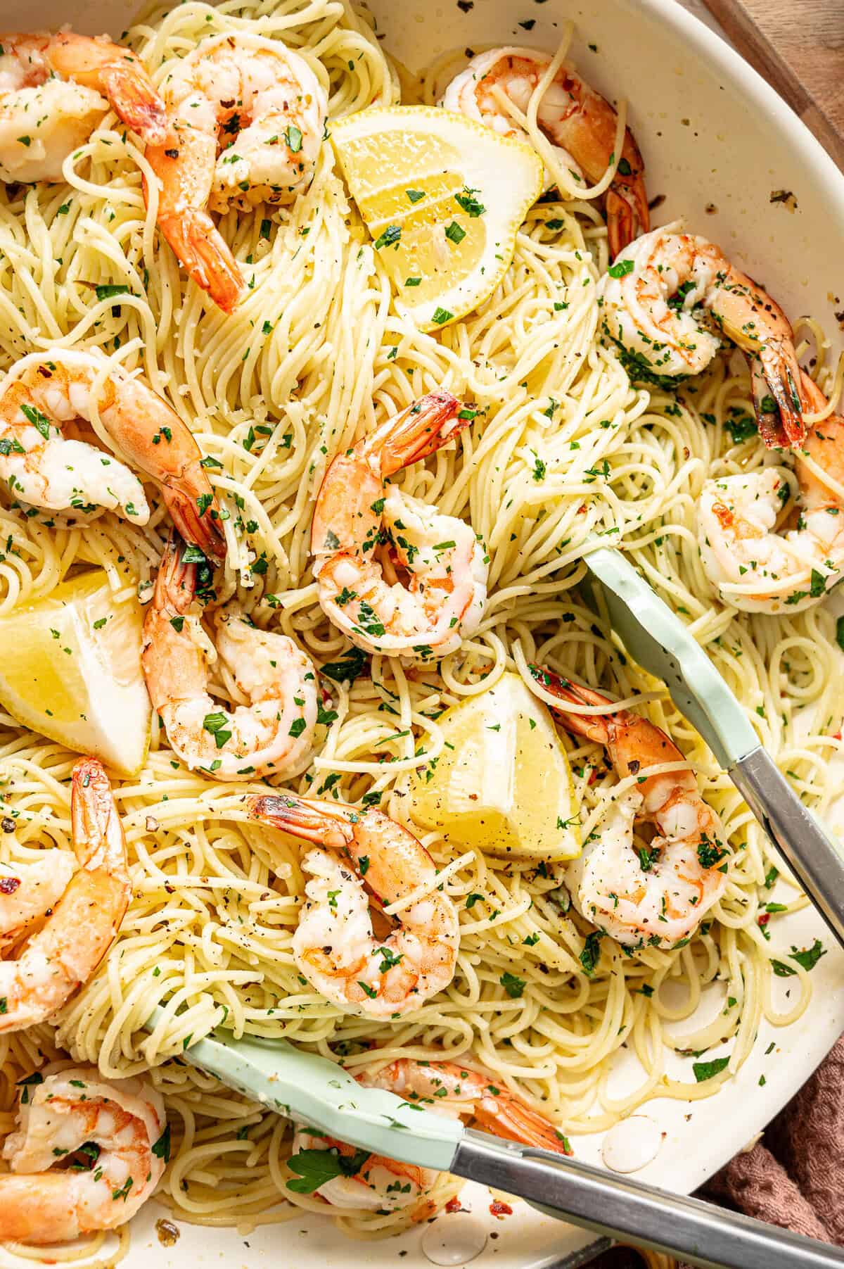 Tongs serving shrimp scampi pasta from a pan.