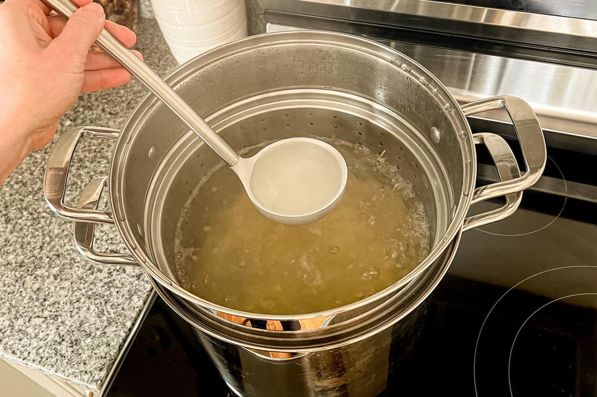 A ladle removing some pasta water to reserve for later steps in shrimp scampi pasta.