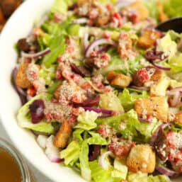 Italian house salad with a bowl of croutons and a jar of dressing next to it.