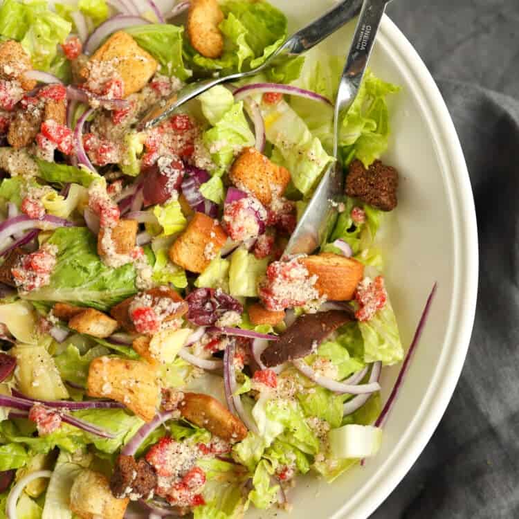 Italian house salad with homemade Italian dressing being served with stainless steel salad tongs.